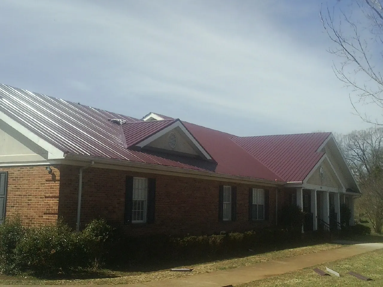 Red metal roof with gabled entries on a long brick building, from a Hail Damage Roof Repair job in Nevis
