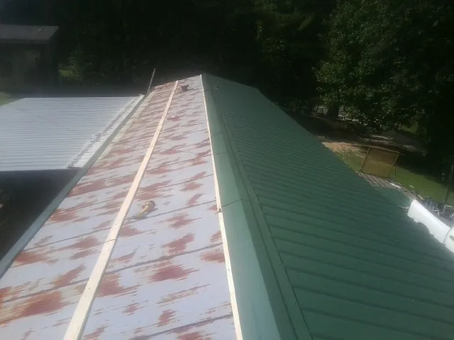 Old rusted panels beside newly installed green metal roofing — Wind Damage Roof Repair by Roofing Brothers in Nevis