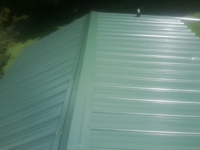 New green metal panels meeting at the ridge of a roof — Flat Roof Repair work by our crew in Nevis