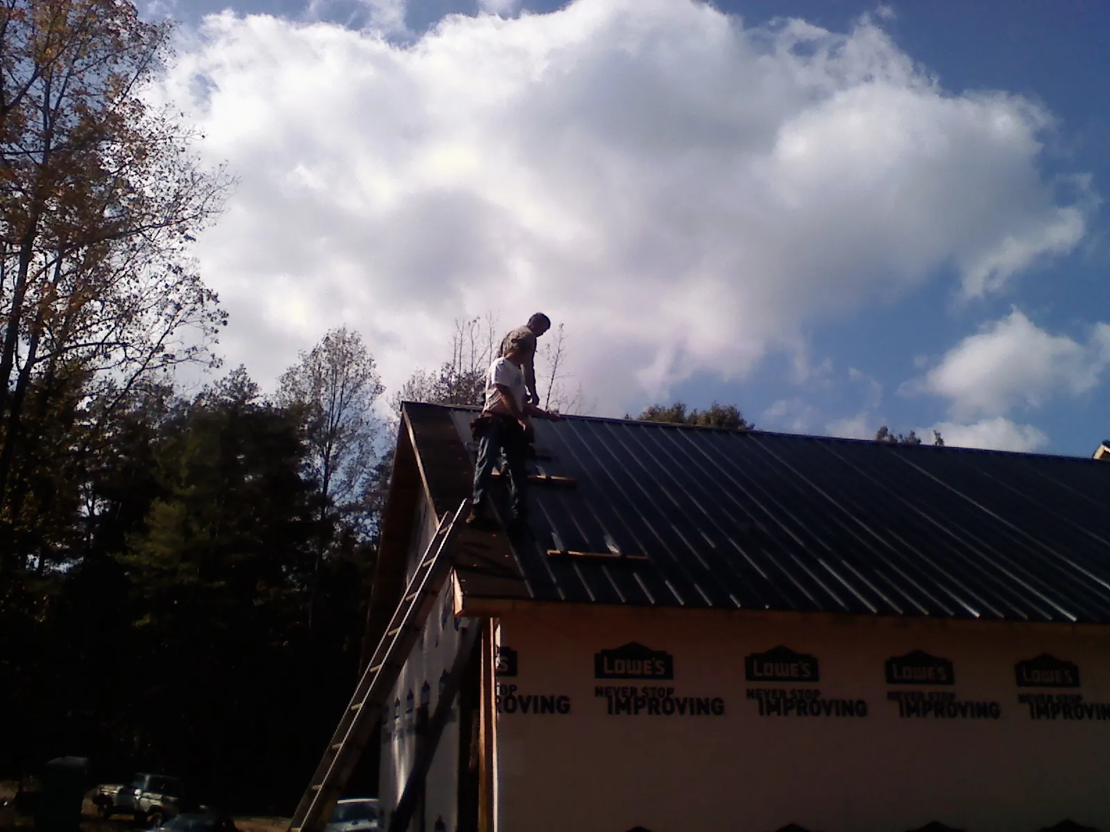 Roofer fastening dark metal panels high against a cloudy sky, from a Roof Inspection job in Nevis