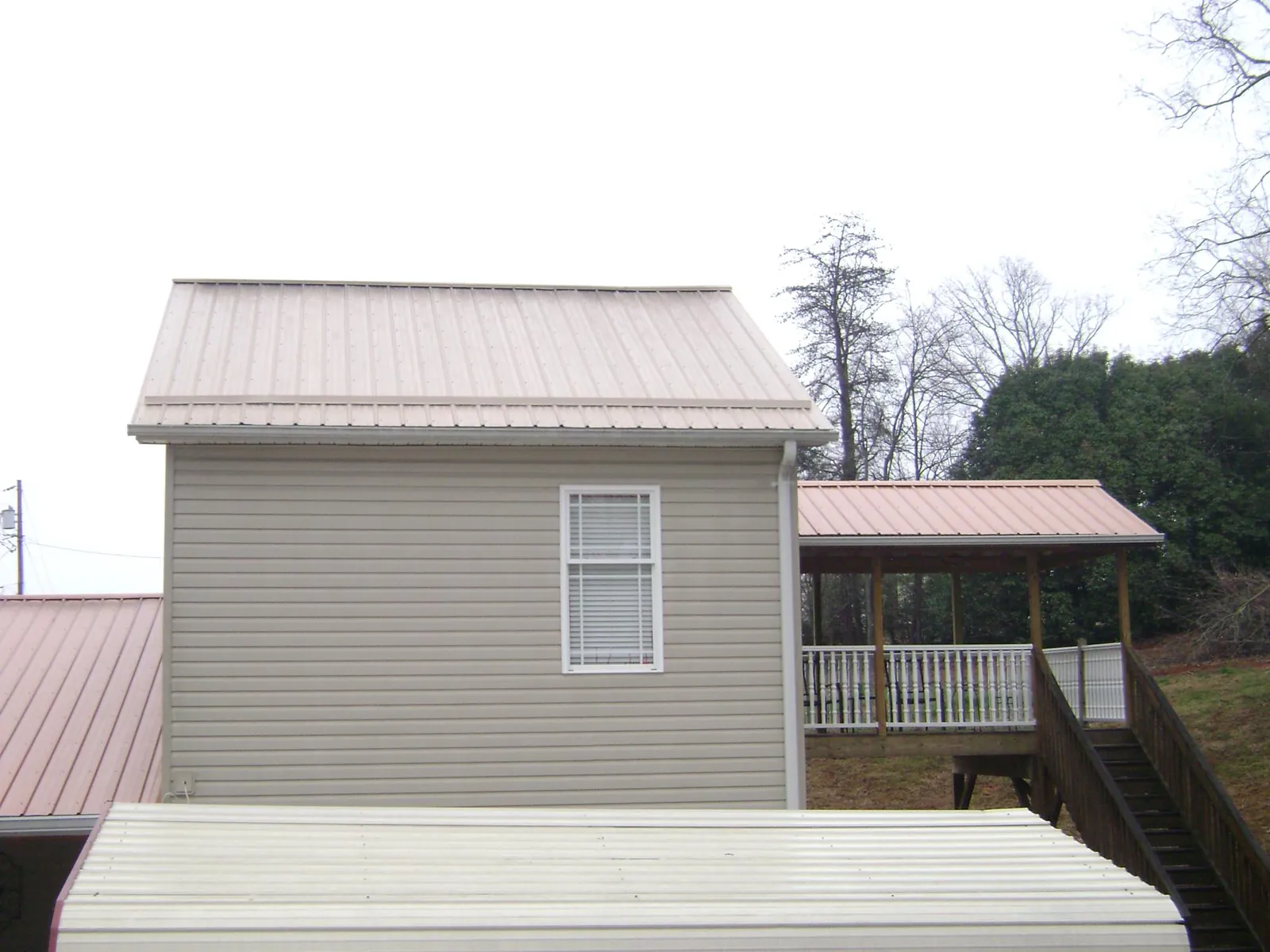 Tan metal roofs on a two story addition and attached porch, from a Roof Replacement job in Nevis